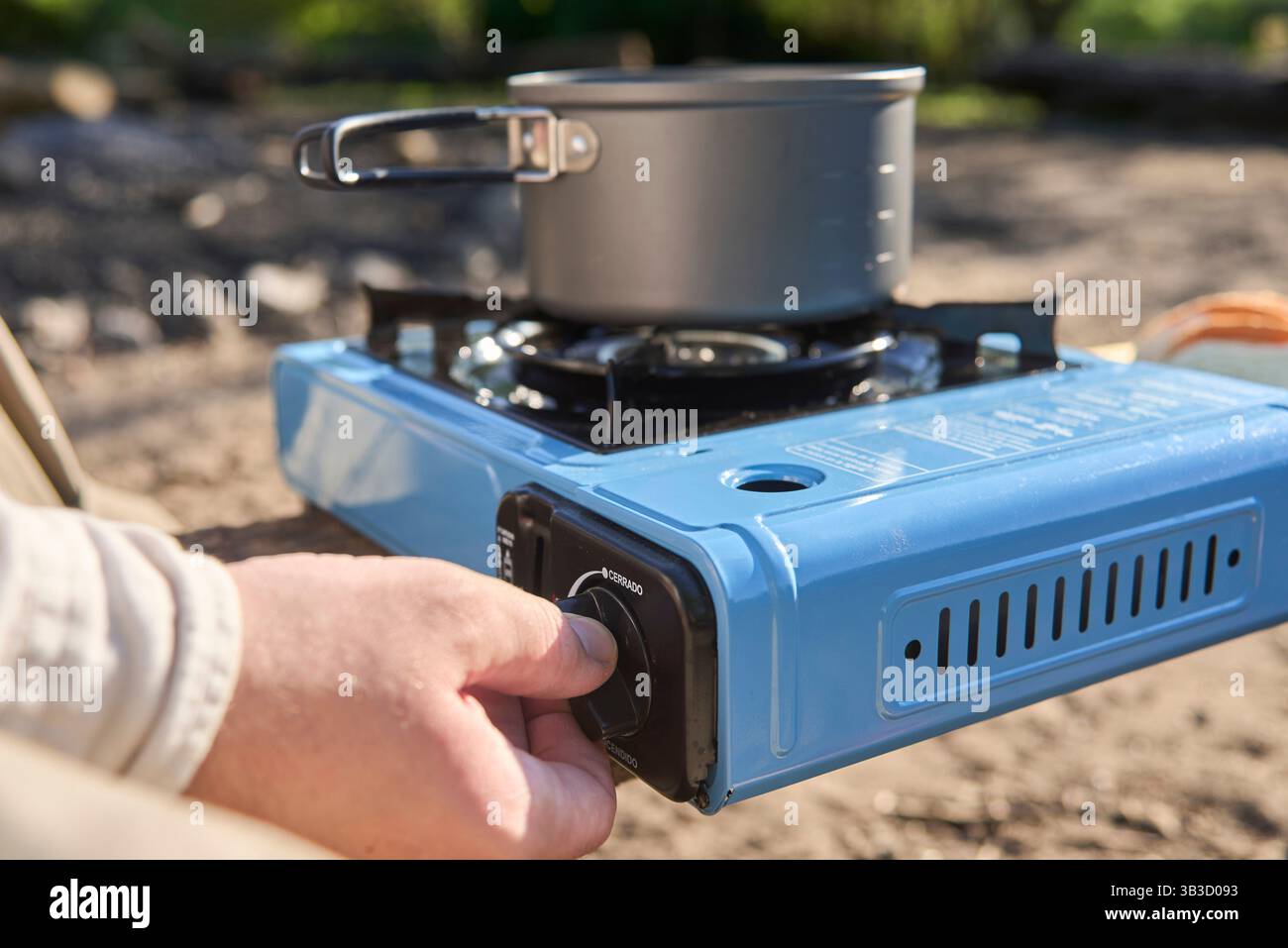 Viaggiatore irriconoscibile che cucina all'aperto mentre campeggia in un campeggio naturale una mattina di sole. Vista ravvicinata della stufa portatile che accende la mano Foto Stock