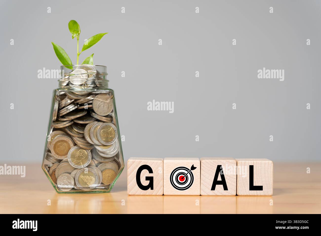Una bottiglia di vetro piena di monete e blocchi di legno e la parola "OBIETTIVO" simboleggia la crescita finanziaria e la pianificazione futura. Obiettivi di raggiungimento fissati. Foto Stock