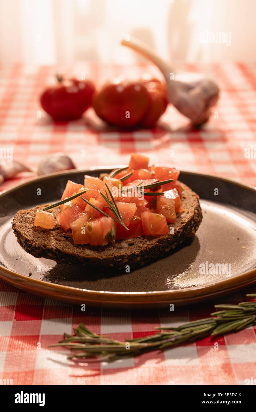 Bruschetta tradizionale con pomodori a dadini e rosmarino fresco servita su un rustico tavolo in legno, concetto di antipasto mediterraneo. Foto Stock