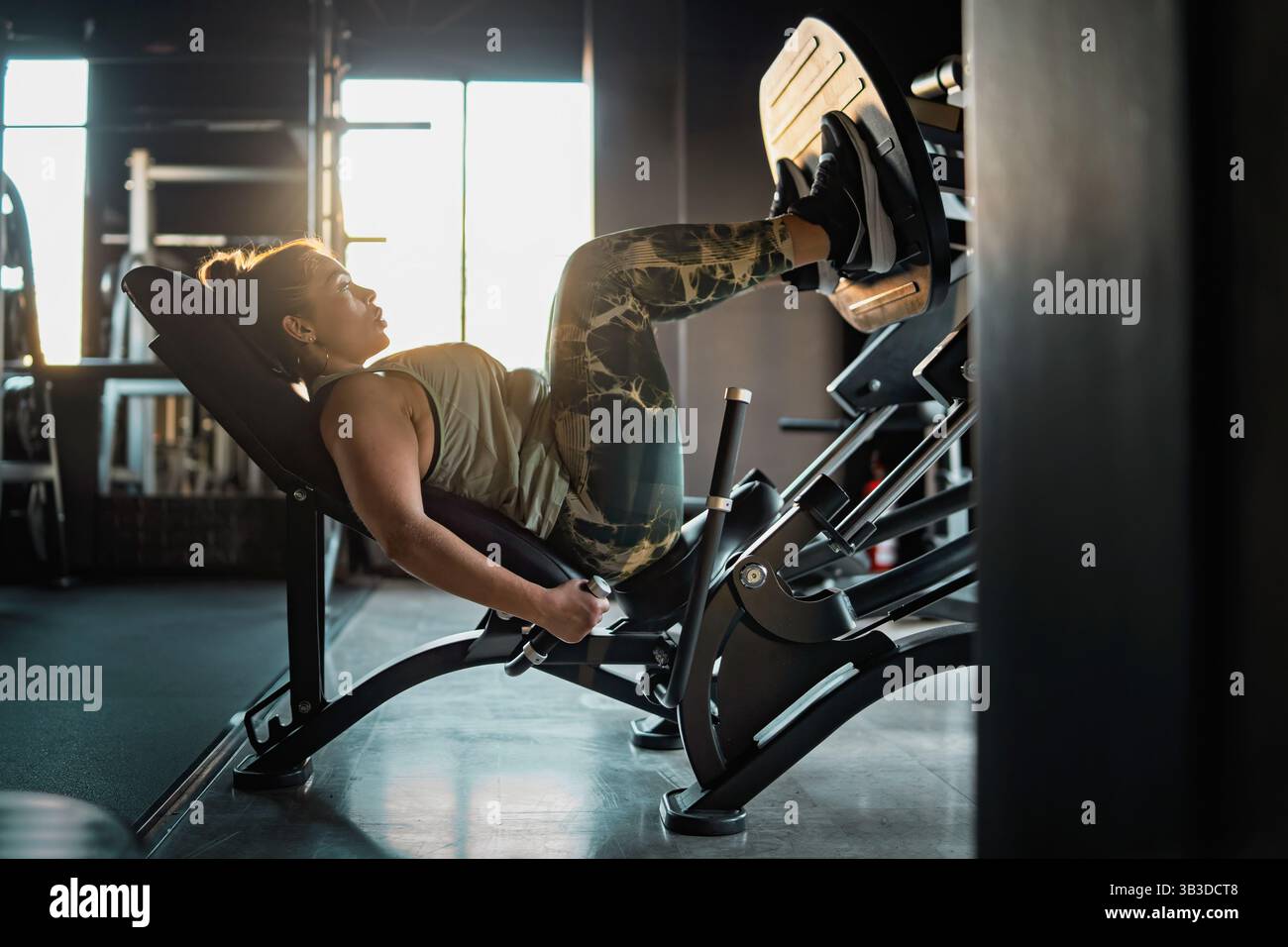 Giovane donna sicura di sé che si allena con una macchina per il pressacarichi durante l'allenamento in palestra. Concetto di forza, fitness e perseveranza. Foto Stock