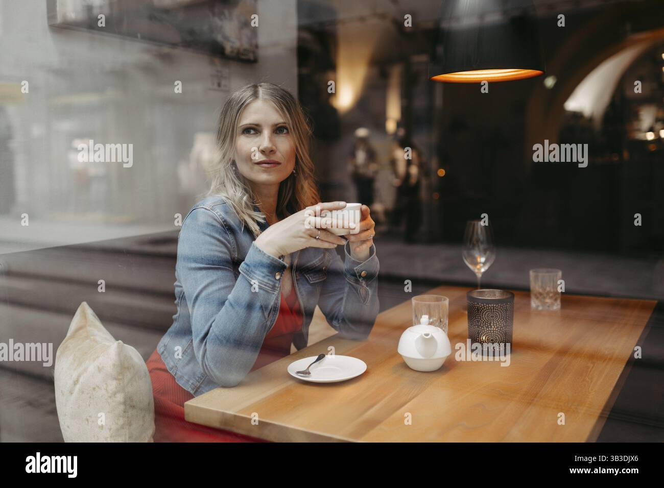 Bionda, donna attraente, 40+, seduta in una caffetteria vicino alla finestra Foto Stock
