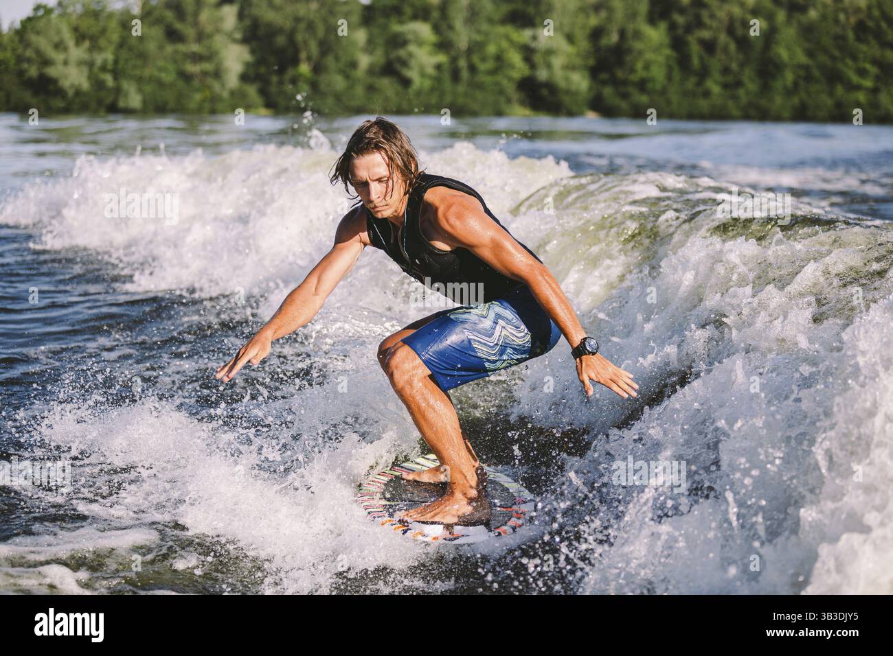 Giovane atletico con lunghi capelli wakesurf sulle onde del fiume in estate sole tempo. Ttheme attività all'aperto in estate. Sport acquatici wakesurf on Foto Stock