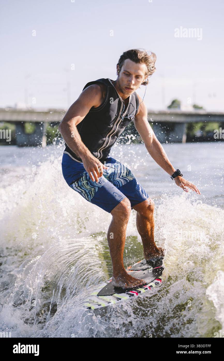 Giovane atletico con lunghi capelli wakesurf sulle onde del fiume in estate sole tempo. Ttheme attività all'aperto in estate. Sport acquatici wakesurf on Foto Stock