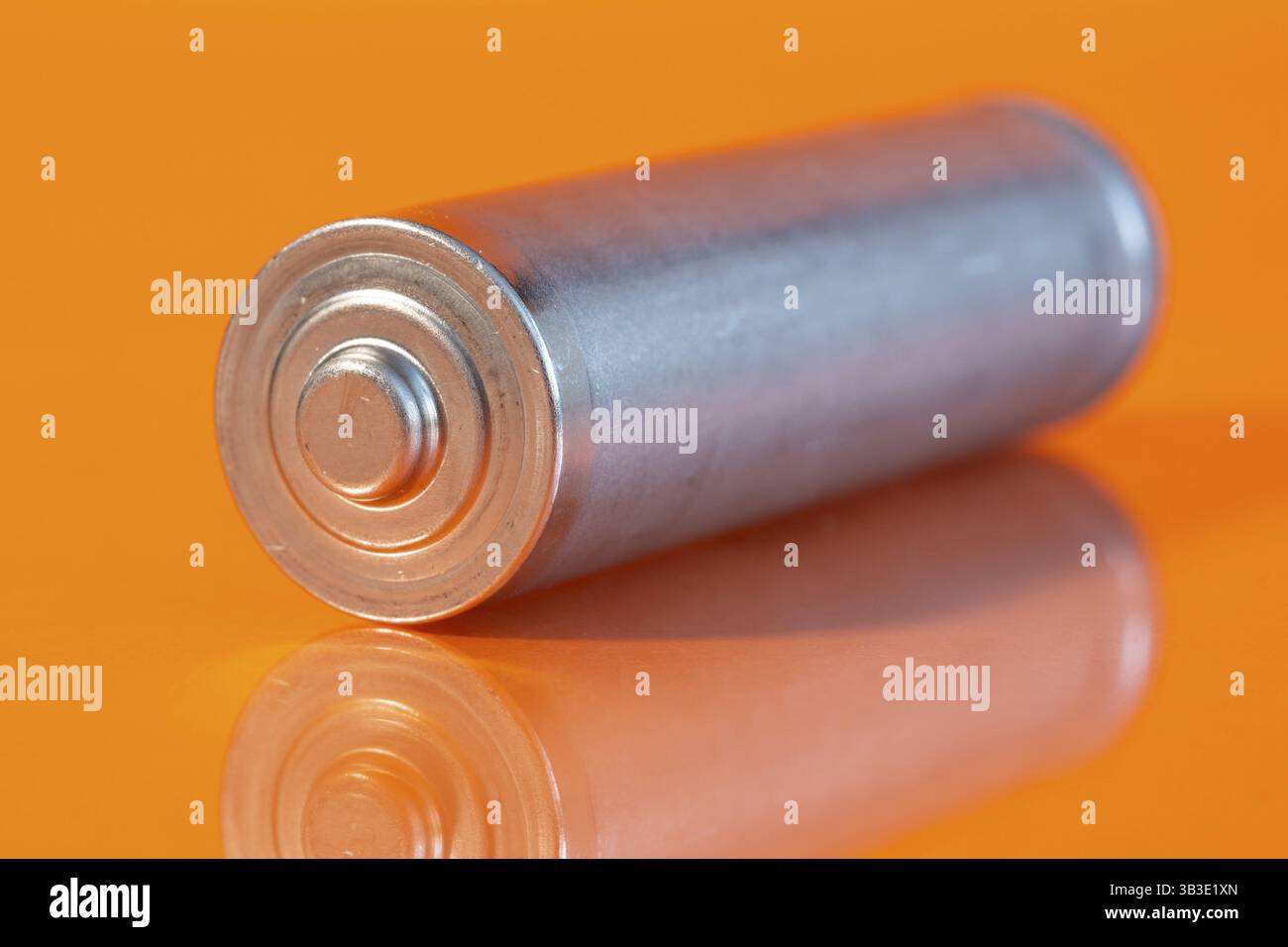 Una singola batteria alcalina AA usata è visibile su una superficie arancione riflettente. Vista laterale ravvicinata dal lato positivo della batteria Foto Stock
