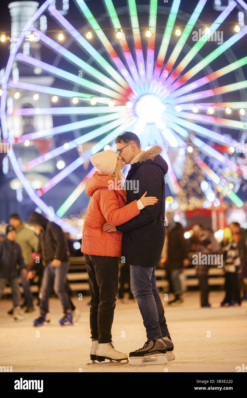 Una giovane coppia caucasica trascorre il Capodanno e le vacanze di Natale in modo attivo e sportivo sull'arena di ghiaccio della città sulla piazza della città. Ro Foto Stock