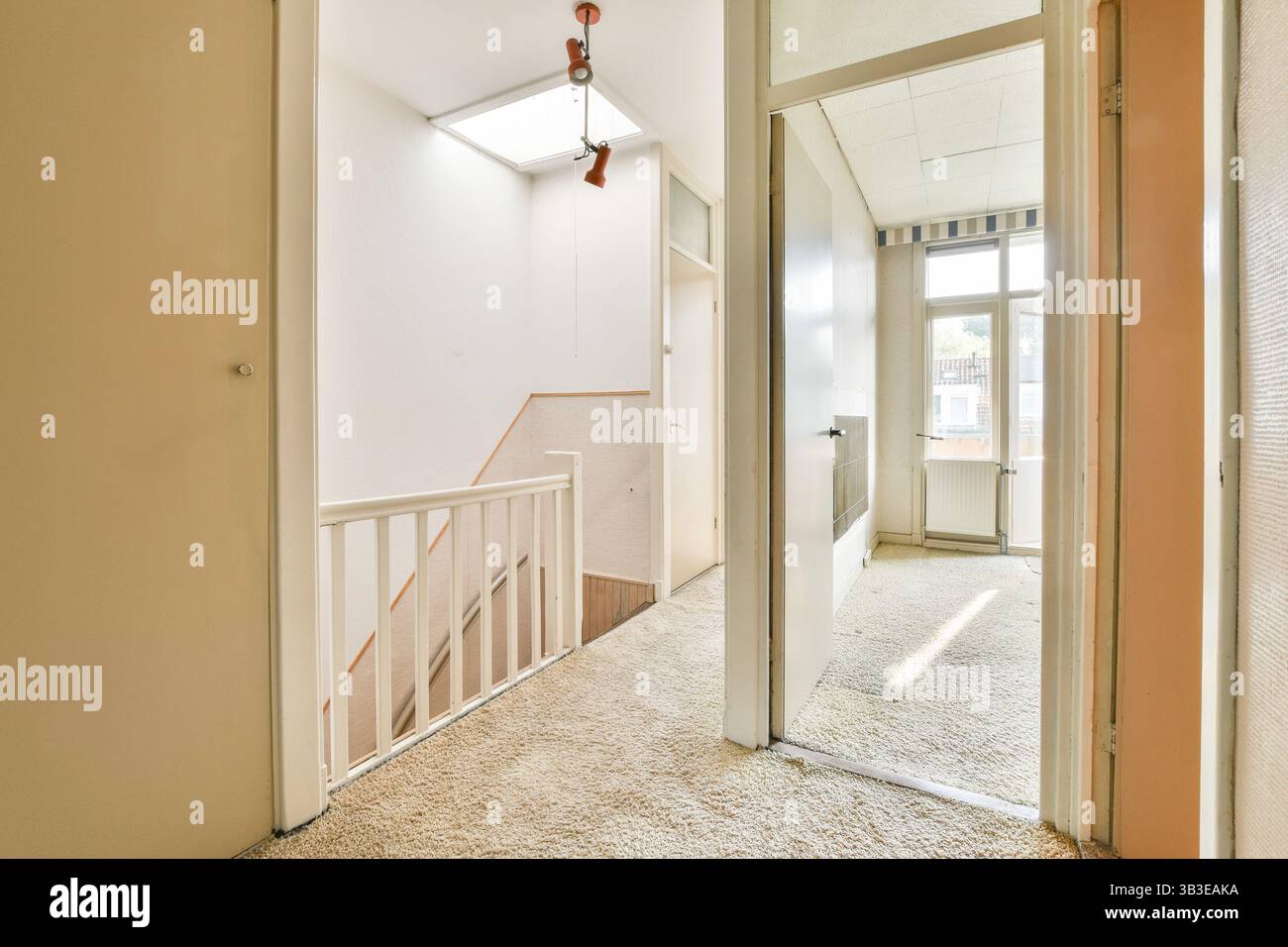 Una scala interna ben illuminata e spaziosa presenta tappeto morbido, ringhiere bianche e molta luce naturale che scorre attraverso le finestre, creando un'atmosfera accogliente. Foto Stock