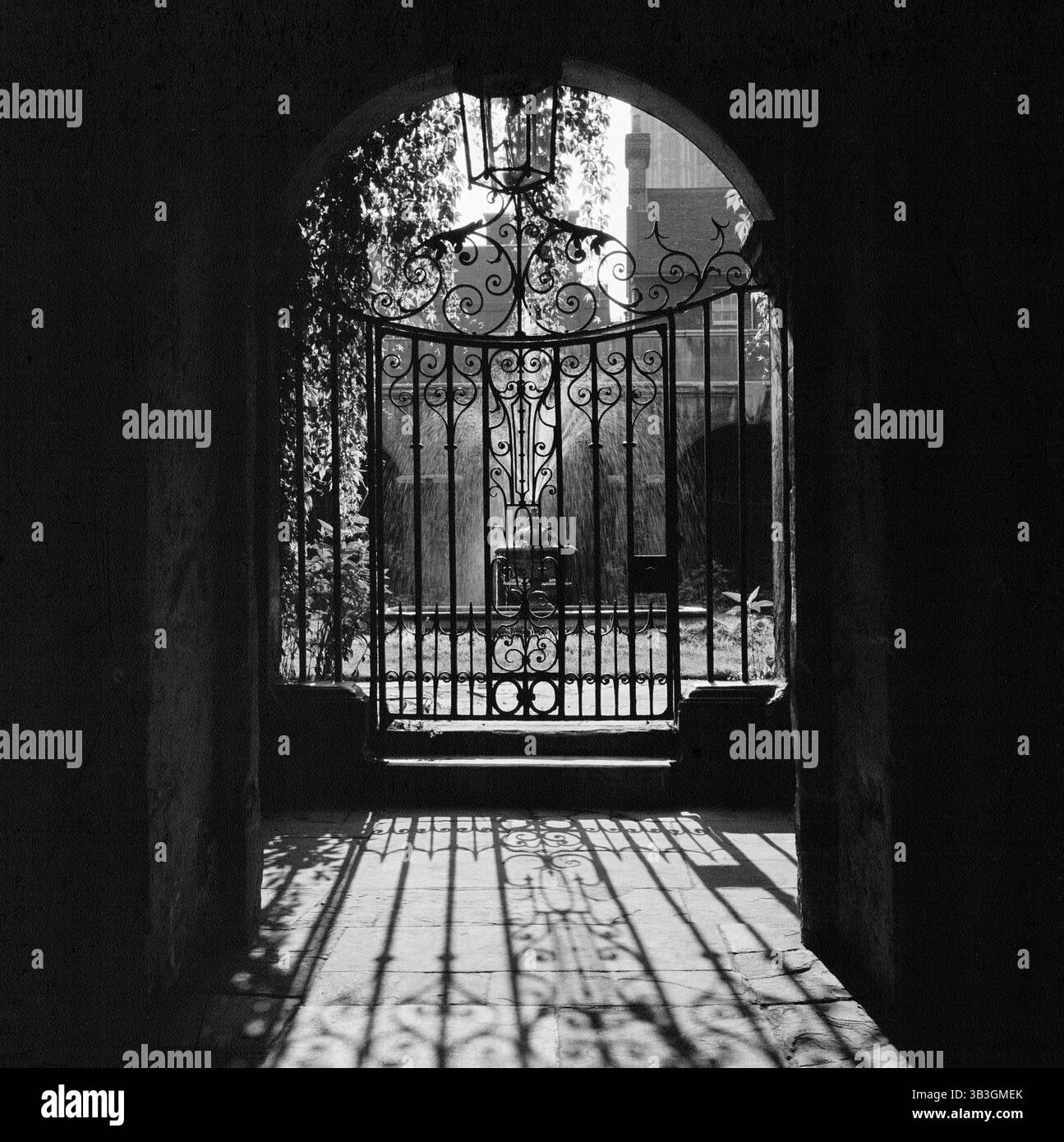 Vista attraverso un cancello decorativo in ferro battuto nel Little Cloister dell'Abbazia di Westminster, Londra, 1946-1999; mostra la fontana nel cortile centrale. Foto Stock