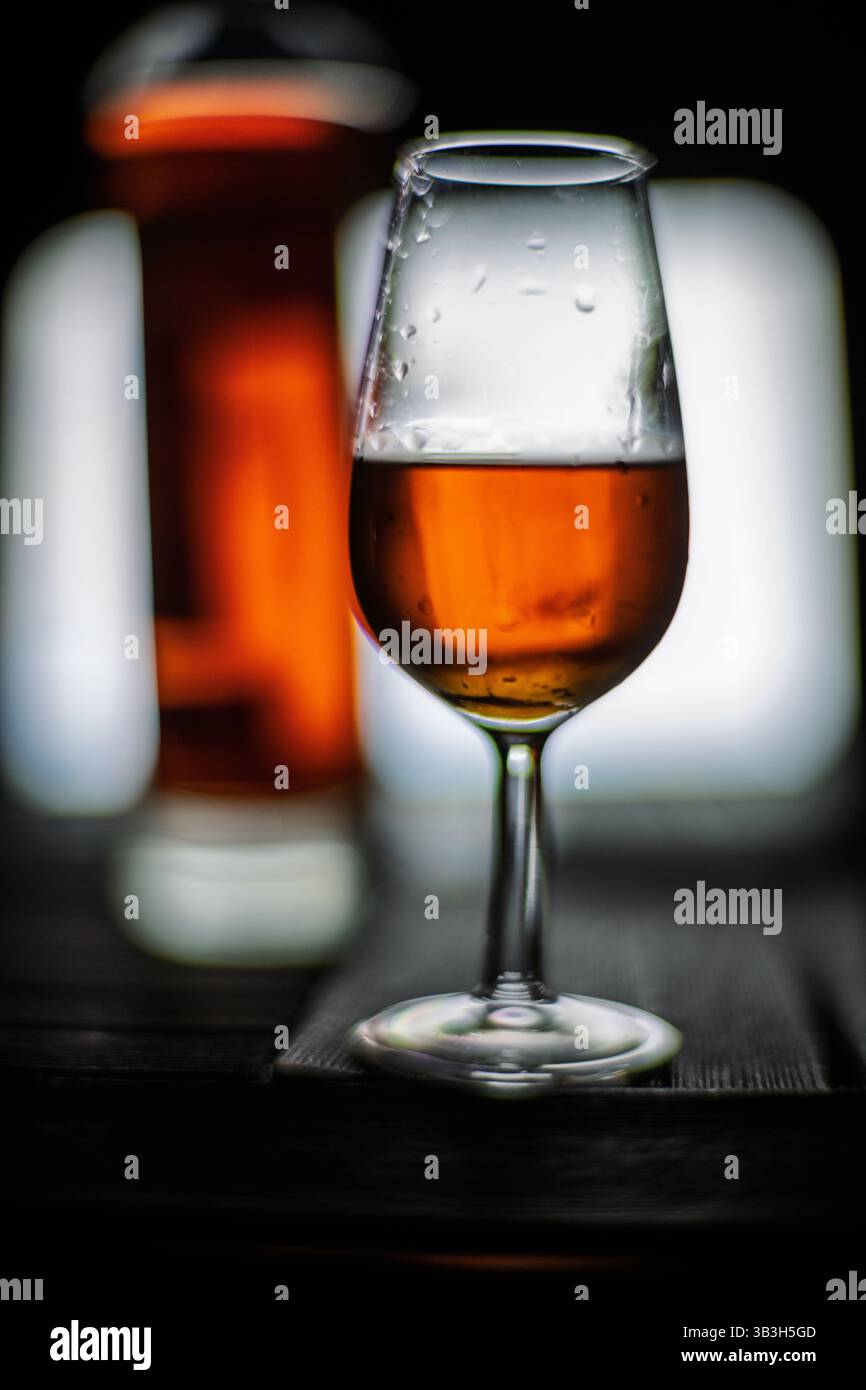 Un bicchiere pieno di sherry palo cortado si siede elegantemente davanti a una bottiglia, mostrando la ricca tonalità ambra su uno sfondo sfocato. Foto Stock