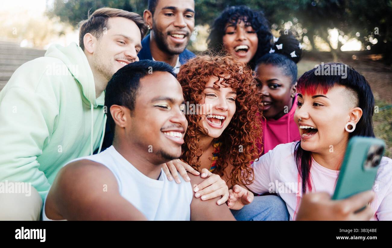 Amici diversi si divertono nel parco cittadino durante le vacanze estive. Un gruppo di persone sorride alla fotocamera per scattare selfie in vacanza Foto Stock