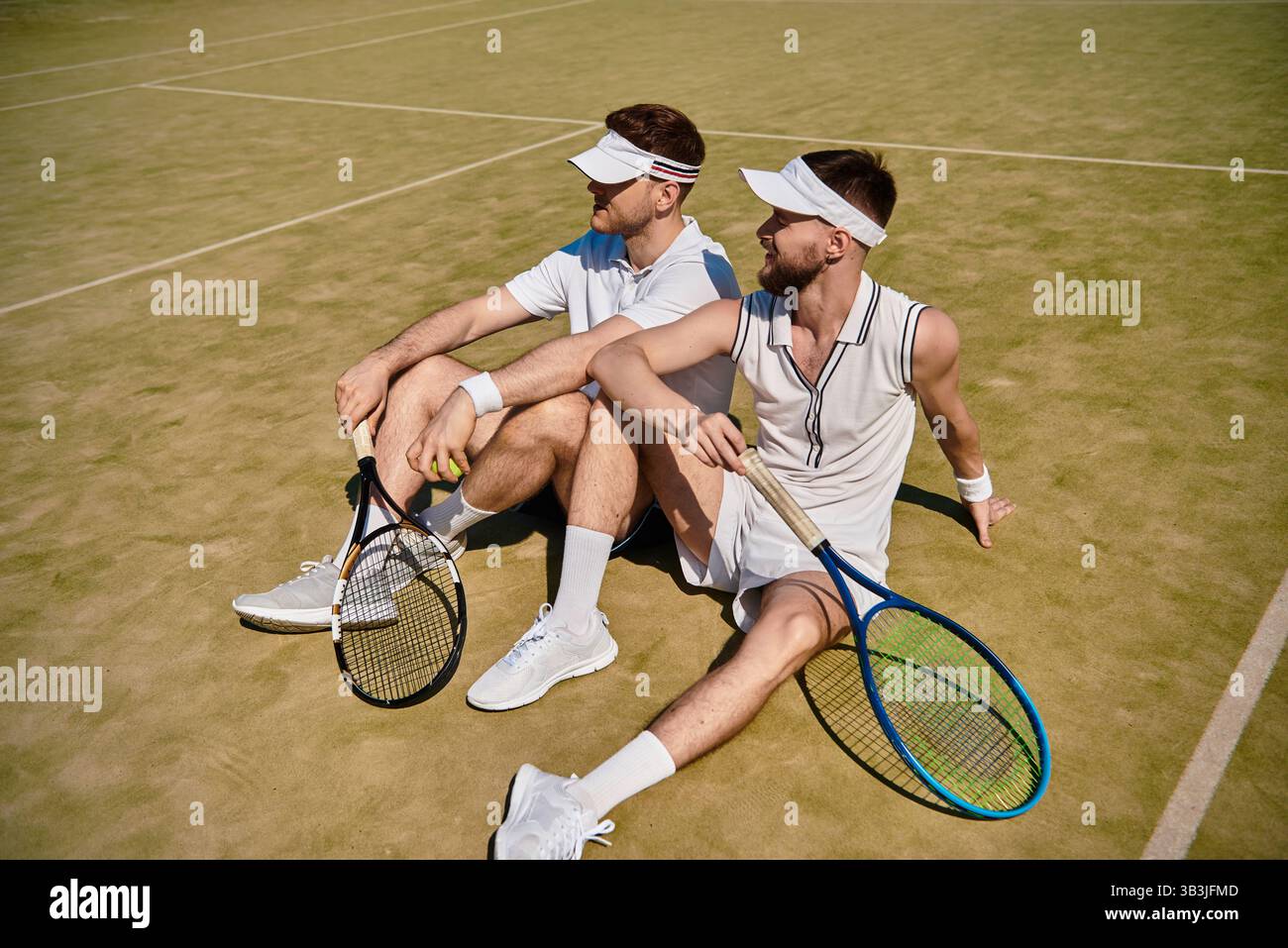 Due uomini si rilassano insieme su un campo da tennis dopo un'emozionante partita sotto il sole estivo. Foto Stock