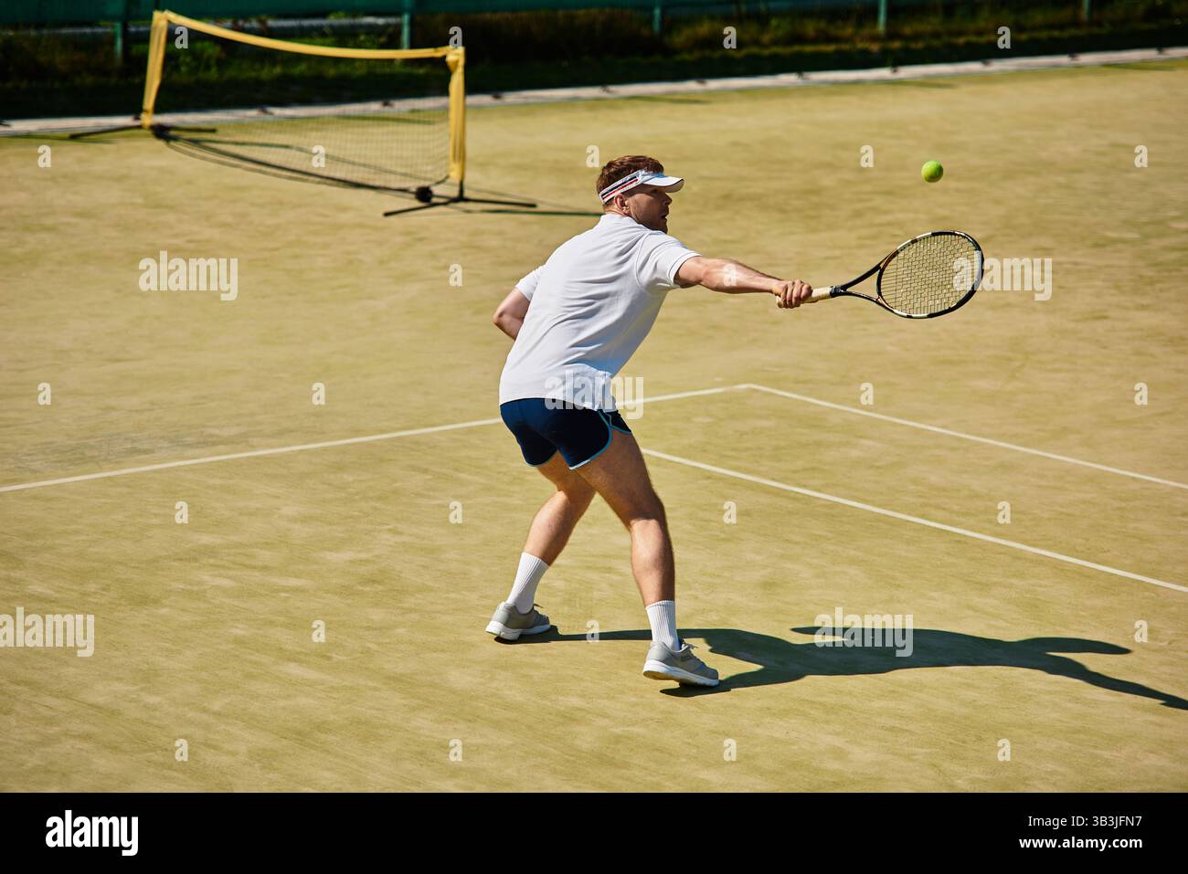 Le vibrazioni estive riempiono l'aria mentre un bell'uomo gioca abilmente a tennis sul campo. Foto Stock