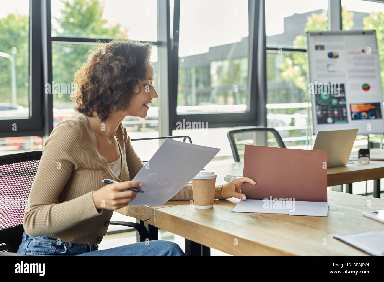 Una donna si impegna a lavorare con cura alla propria scrivania, circondata da moderni elementi d'ufficio e dal verde. Foto Stock