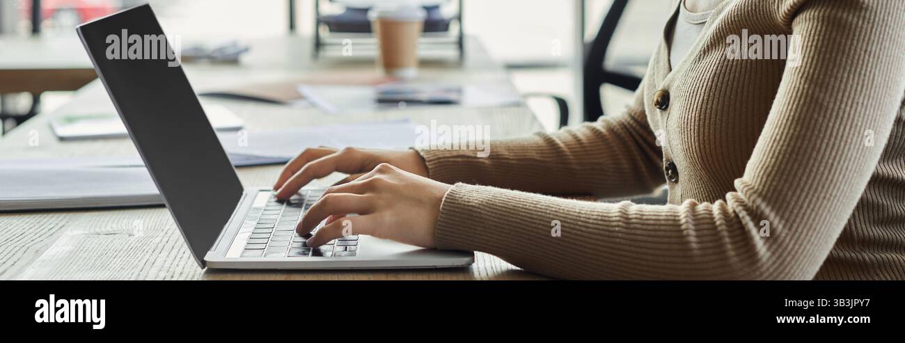 Una persona si impegna con il proprio notebook, immersa in attività in uno spazio di lavoro luminoso e minimalista. Foto Stock