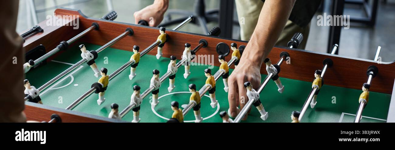 Le mani navigano abilmente sul tavolo da calcio mentre i colleghi si impegnano in una partita vivace in ufficio. Foto Stock