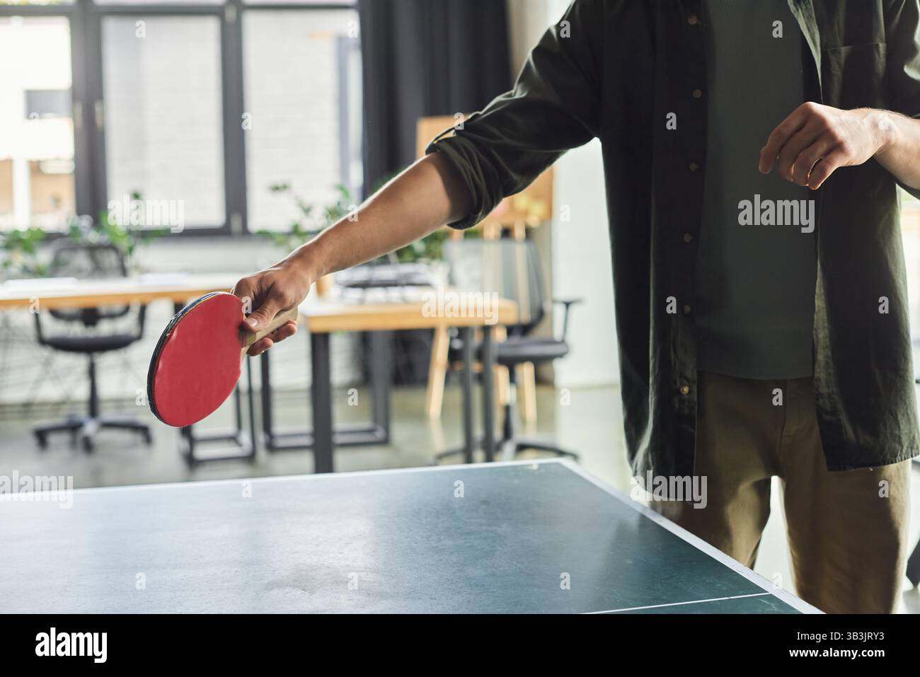 Una persona si prepara abilmente a colpire una palla da ping pong in un ufficio moderno con postazioni di lavoro. Foto Stock