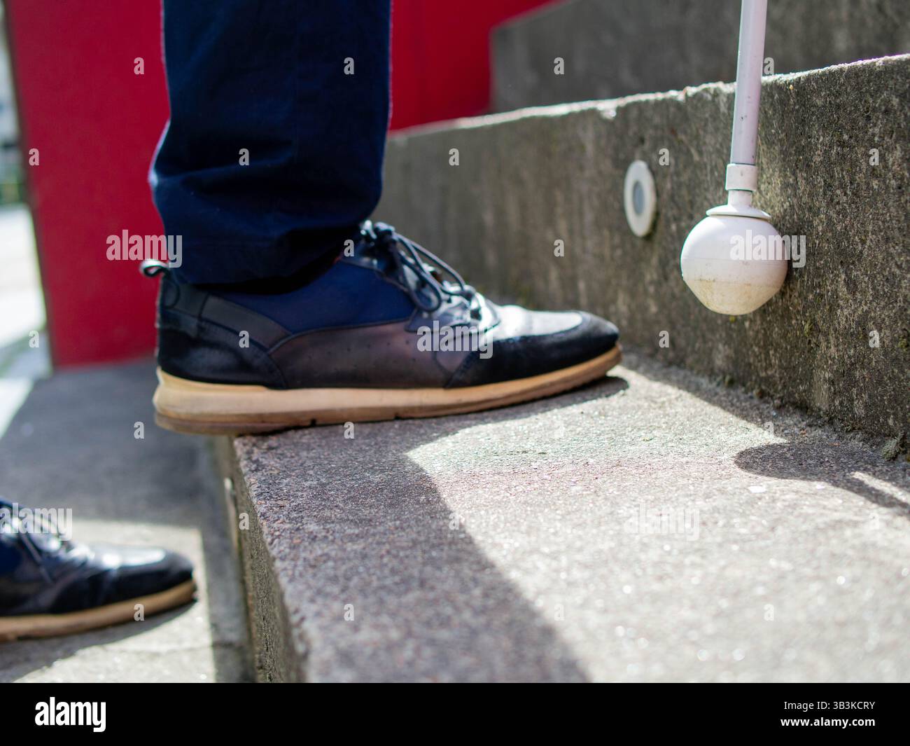 Dettaglio della punta di un bastone bianco usato da un cieco mentre si sale al piano superiore in un parco Foto Stock