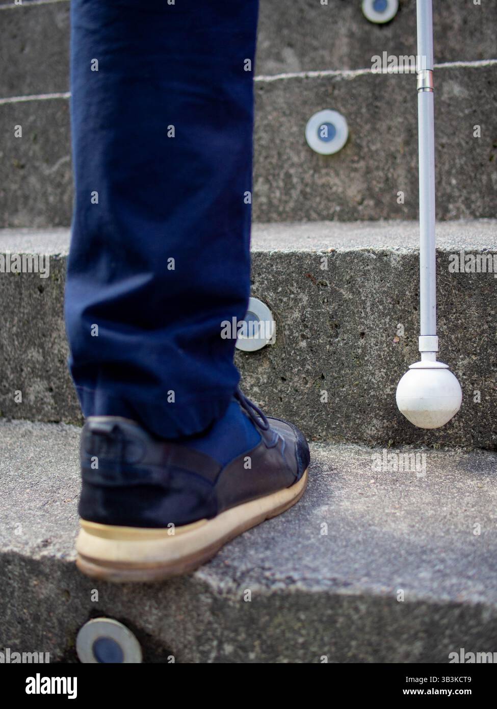 Dettaglio della punta di un bastone bianco usato da un cieco mentre si sale al piano superiore in un parco Foto Stock