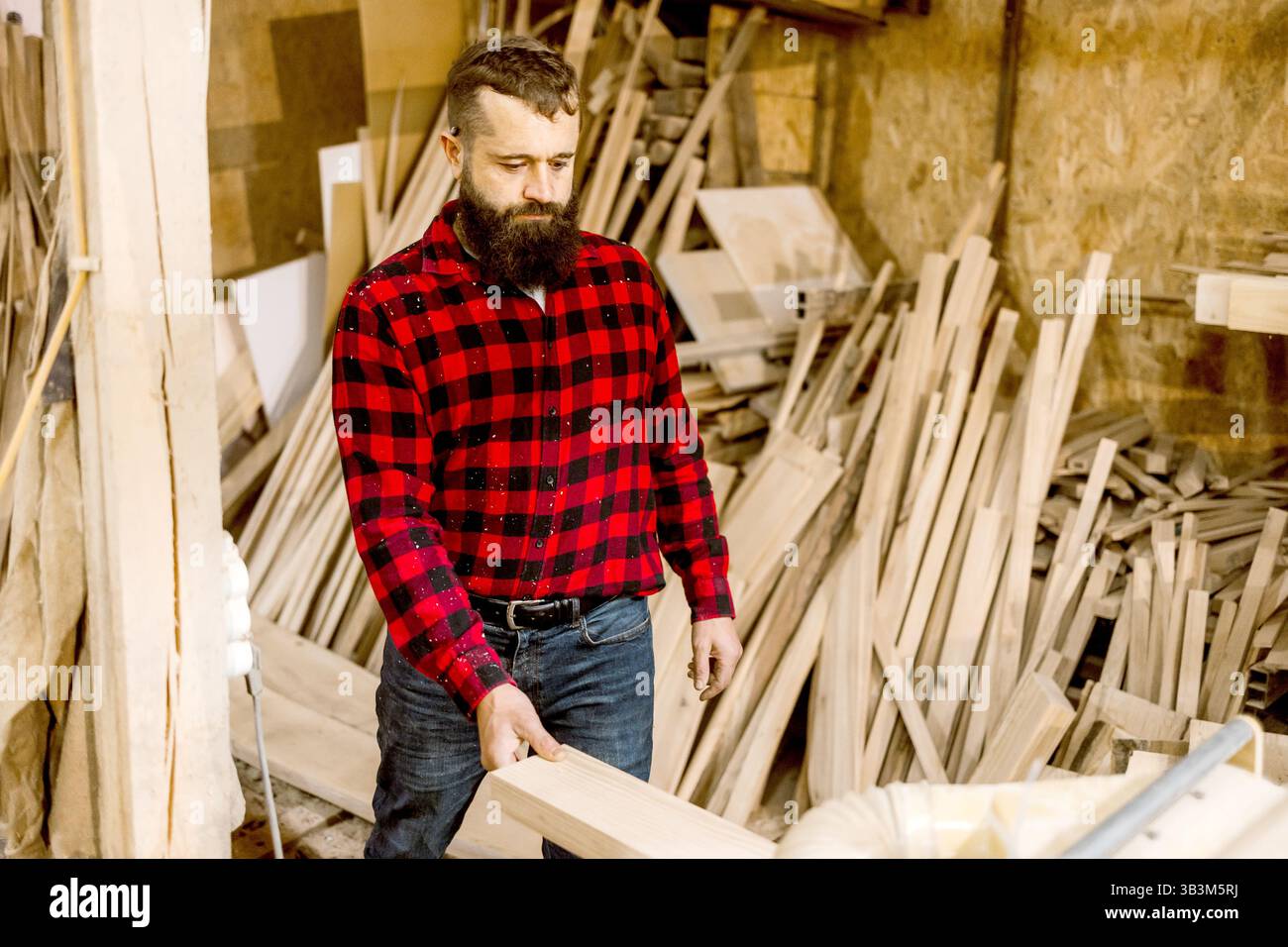 L'artigiano in un negozio di lavorazione del legno seleziona il legno mentre è circondato da materie prime, mostrando abilità e creatività in un ambiente rustico Foto Stock