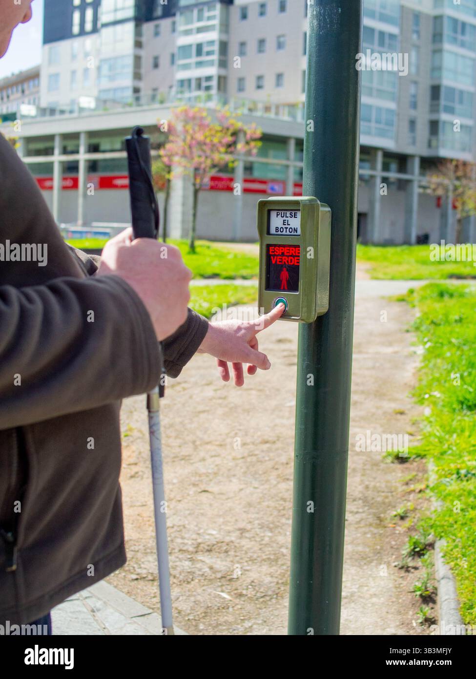 Un cieco che preme il pulsante pedone tattile, in attesa che il segnale audio attraversi la strada in modo sicuro Foto Stock
