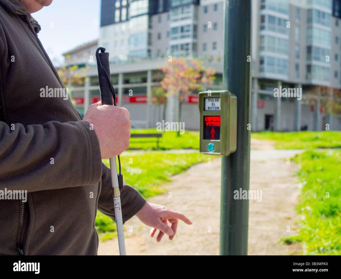 Un cieco che preme il pulsante pedone tattile, in attesa che il segnale audio attraversi la strada in modo sicuro Foto Stock