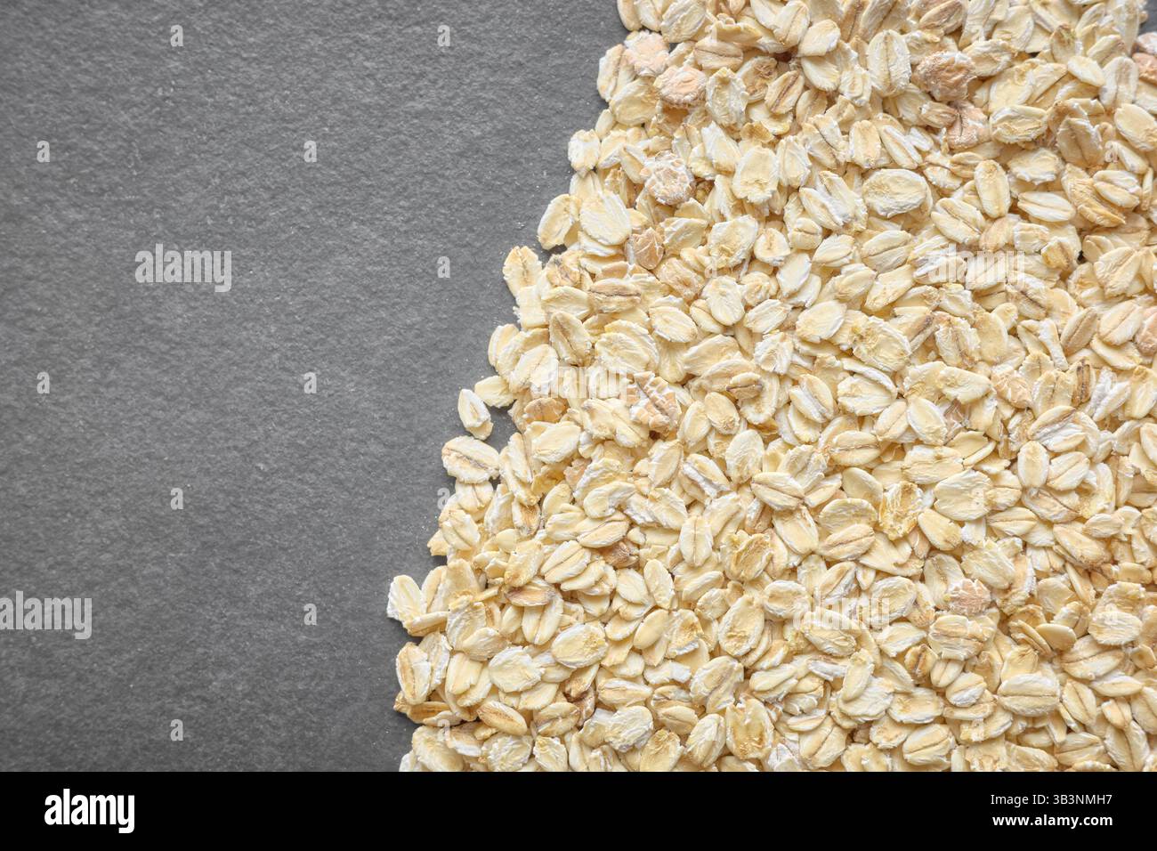 Foto ravvicinata di fiocchi d'avena organici su uno sfondo scuro di ardesia. Foto Stock
