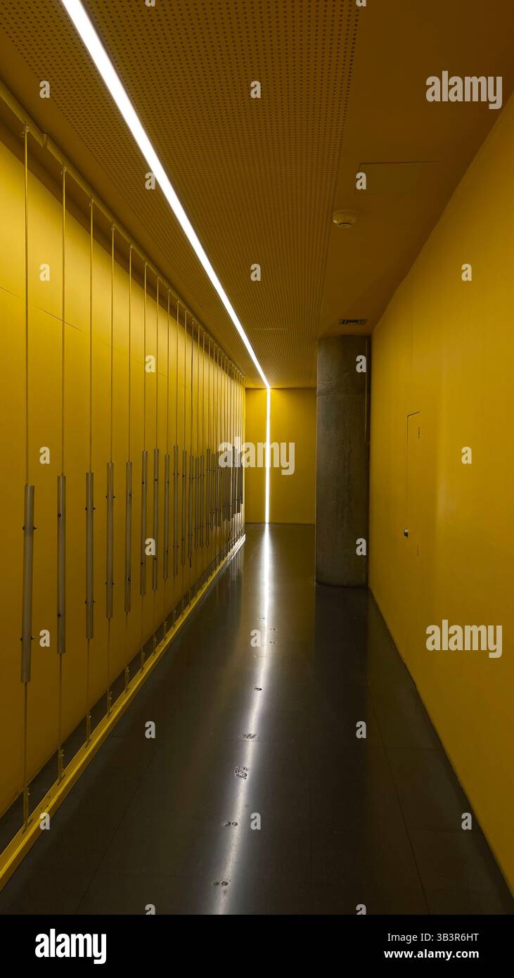 Corridoio minimalista astratto in giallo brillante con illuminazione lineare, design geometrico e pavimento riflettente lucido. Foto Stock