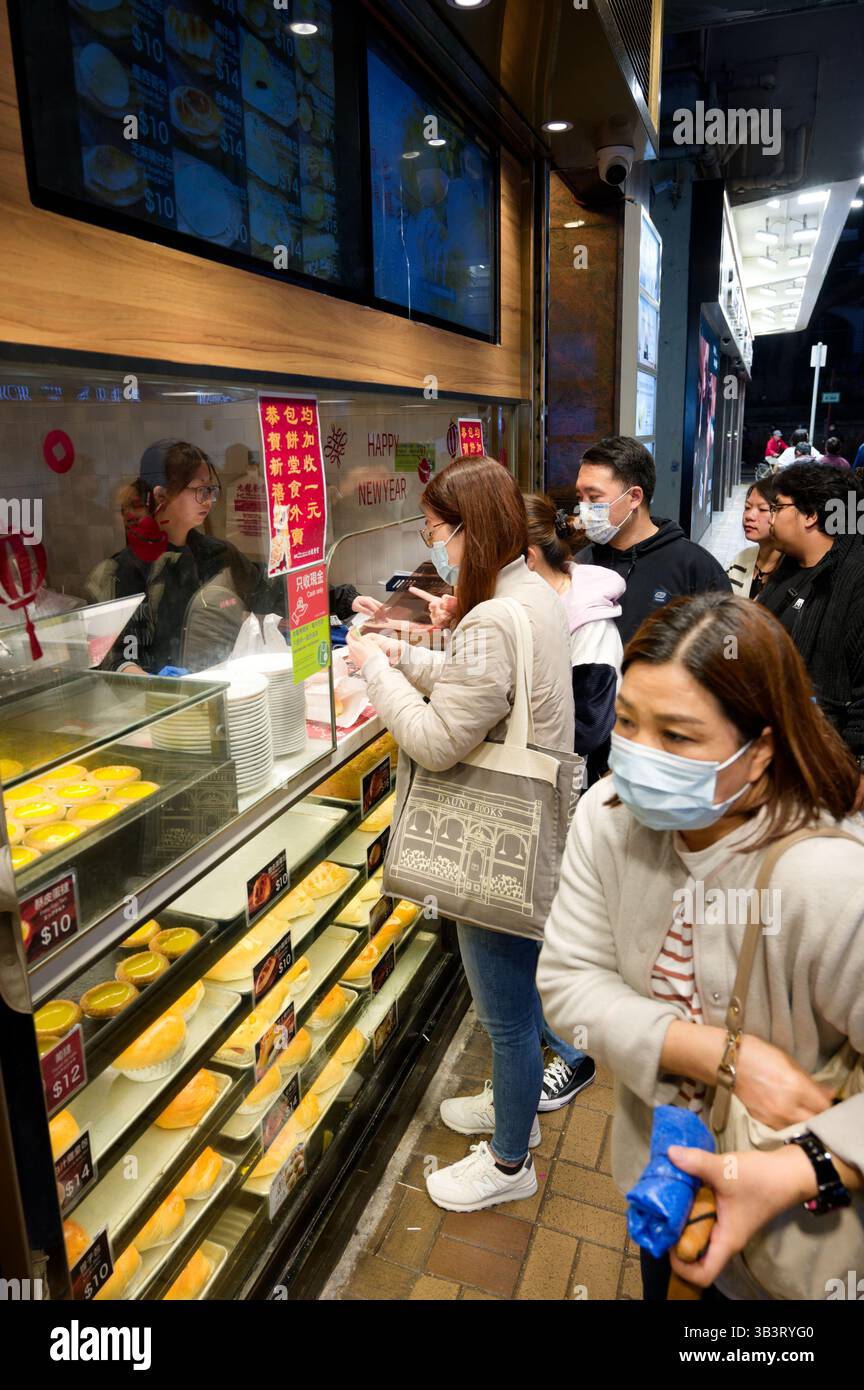 Coda serale presso un'amata panetteria di Hong Kong, dove crostate dorate e panini dolci rubano lo spettacolo Foto Stock