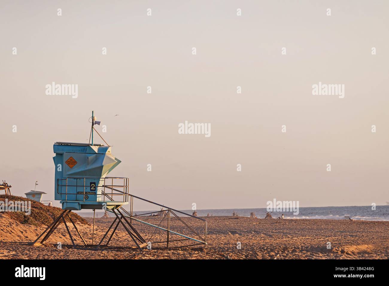 La torre del bagnino sorveglia la tranquilla spiaggia al tramonto con dolci onde che lambiscono sulla riva Foto Stock