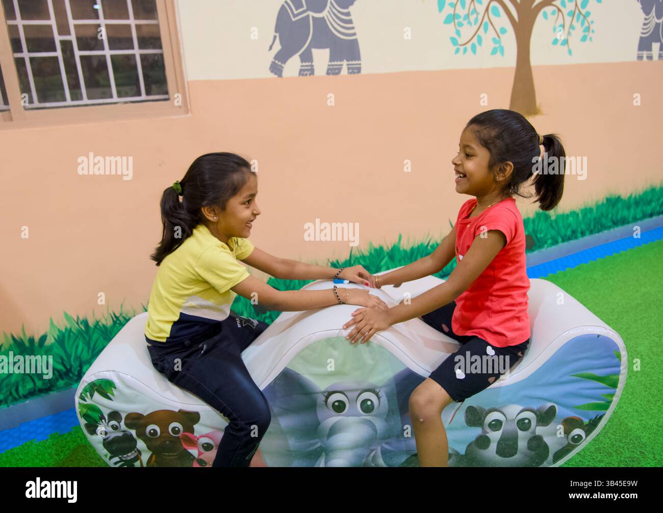 Due ragazze si divertono a giocare in un colorato giro a tema animale in un'area giochi al coperto piena di vivaci decorazioni. Foto Stock