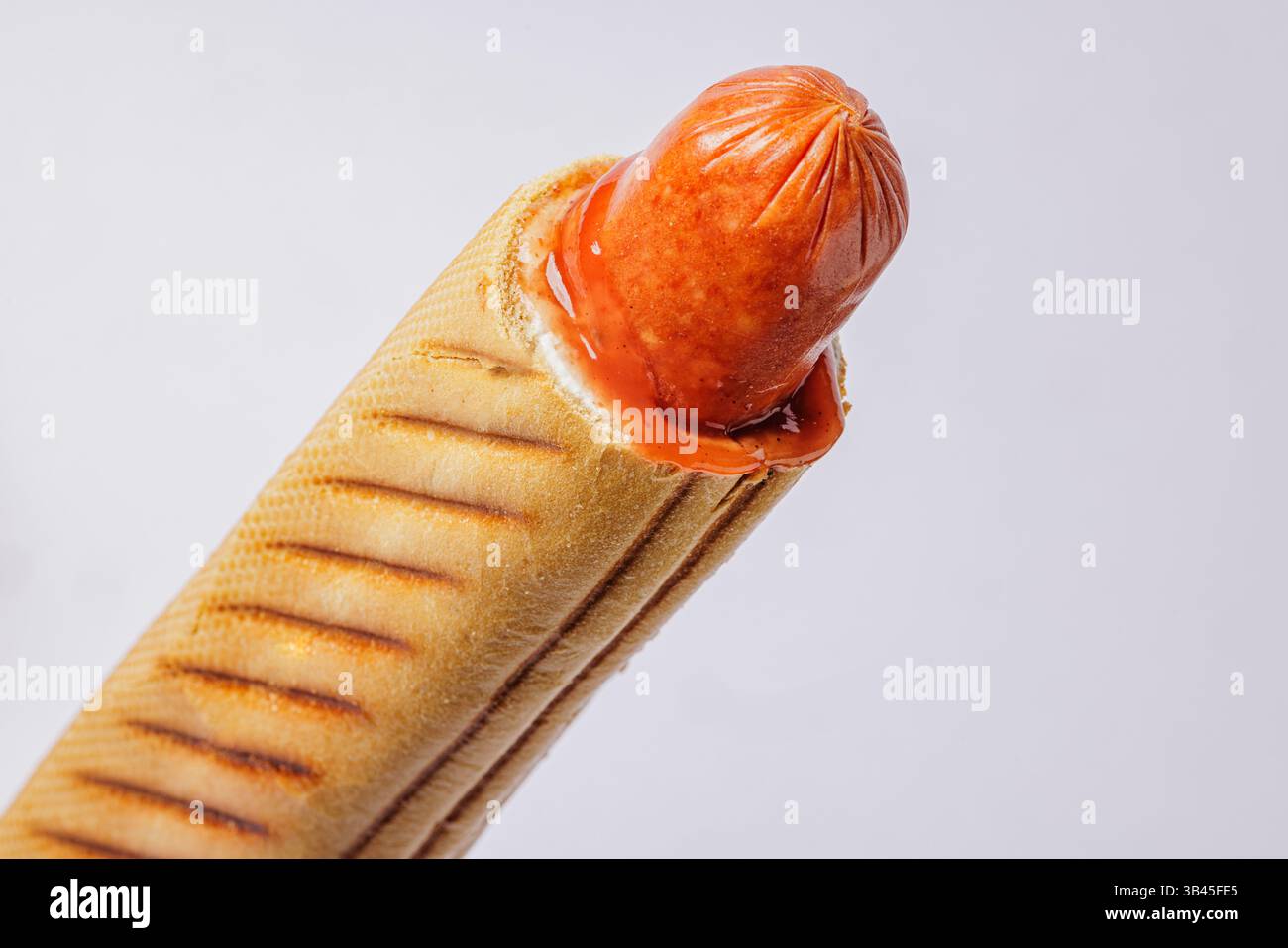 Hot dog grigliato in panino tostato con ketchup, isolato su sfondo bianco, concetto di primo piano di fast food. Foto Stock