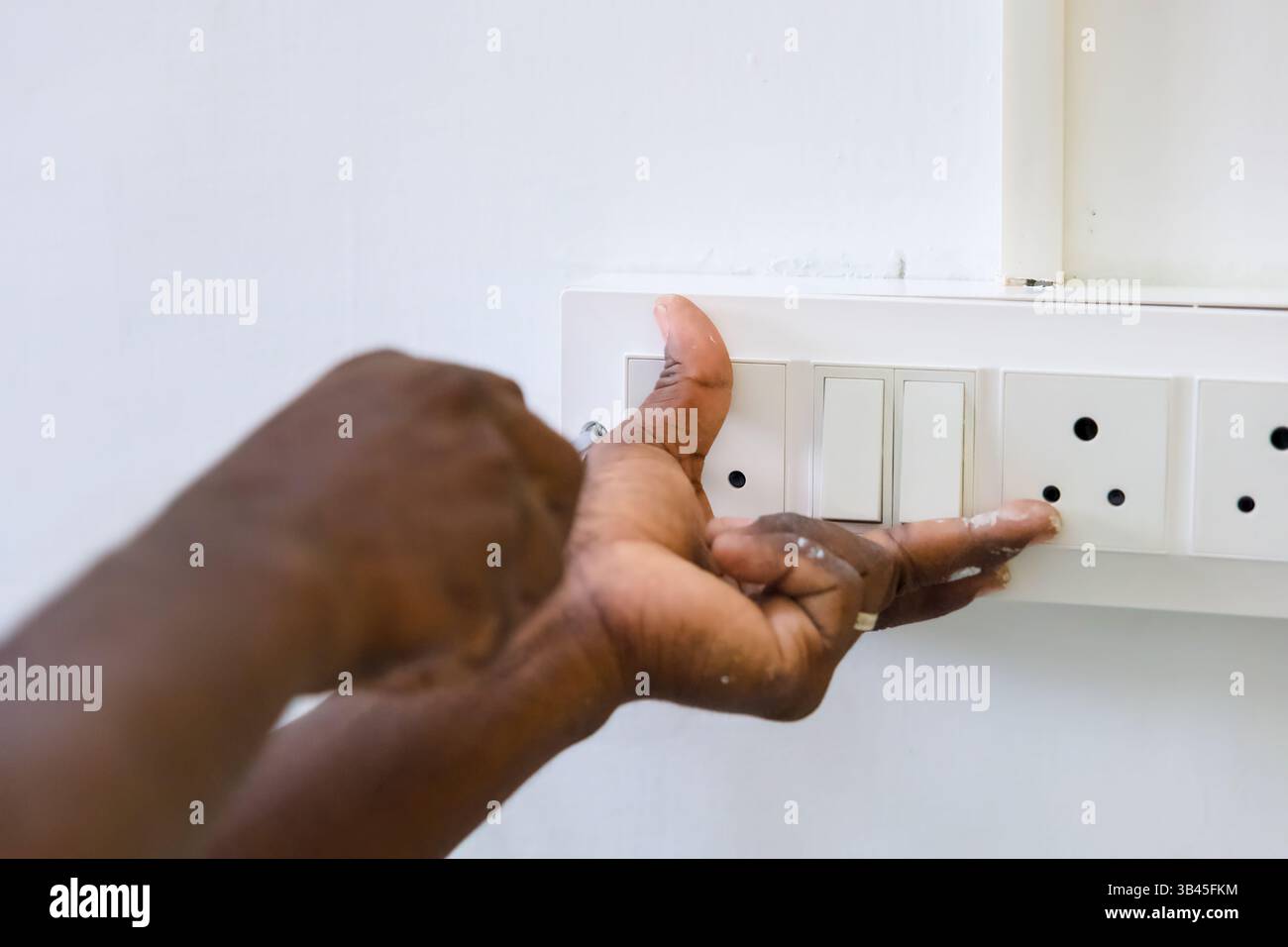 Personale esperto lavora per fissare una presa elettrica durante il giorno in una stanza ben illuminata, mostrando attenzione ai dettagli. Foto Stock