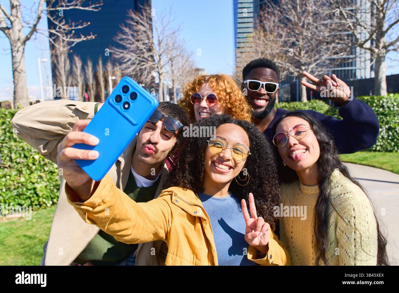 Cinque allegri giovani amici catturano insieme un momento di divertimento, scattando un selfie in un vivace parco cittadino, mostrando la loro diversa amicizia e la loro vita urbana Foto Stock