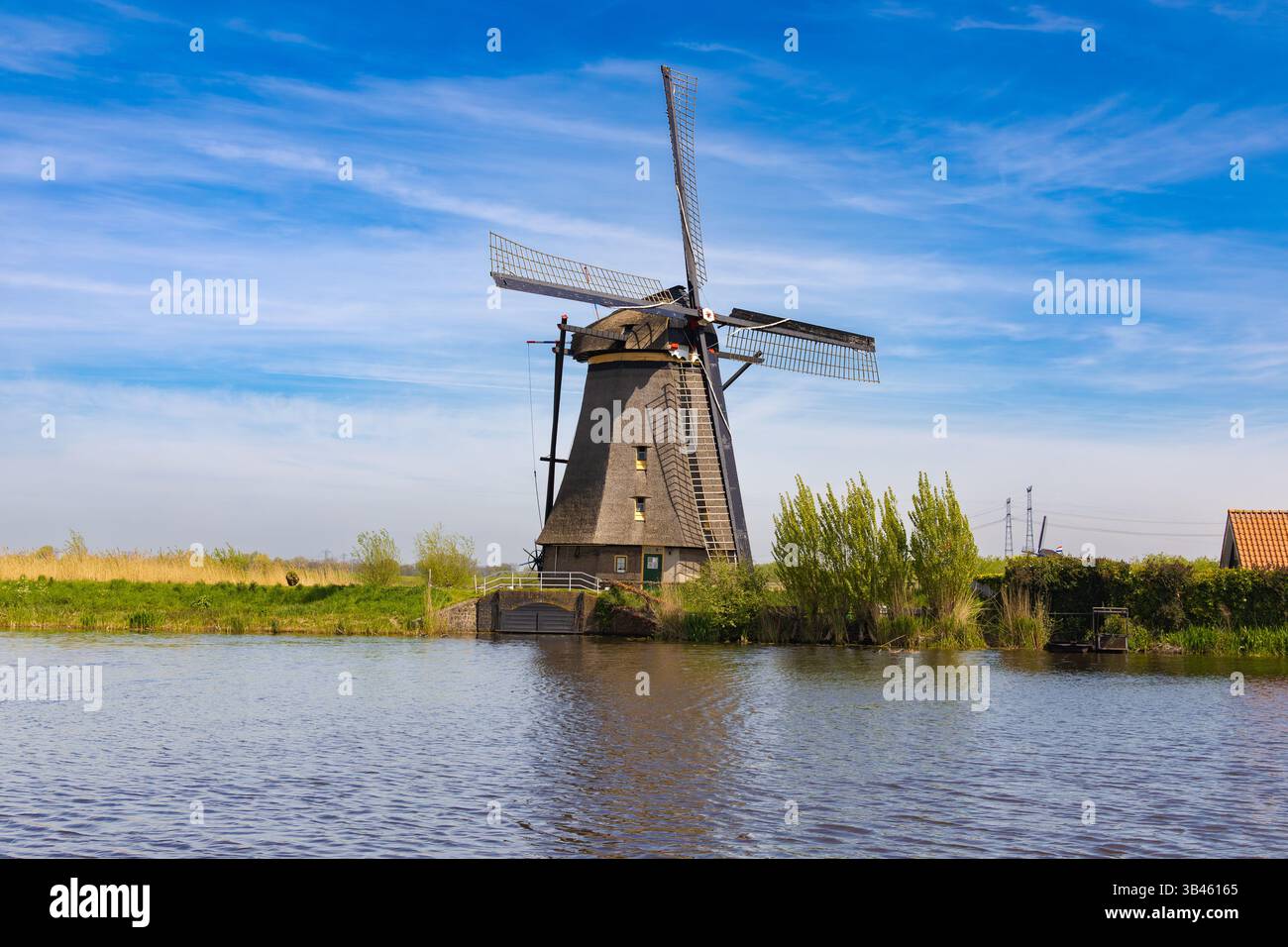 Classico mulino a vento olandese lungo un corso d'acqua a Kinderdijk, Paesi Bassi, con riflessi sull'acqua e nuvole nel cielo. Foto Stock