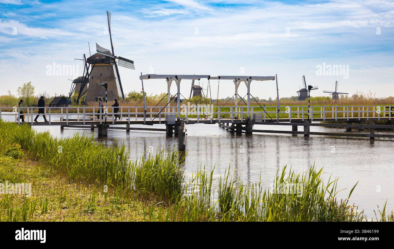 Vista panoramica di Kinderdijk, Paesi Bassi, con storici mulini a vento, un ponte su un corso d'acqua con attraversamento di persone e un vivace paesaggio verde Foto Stock