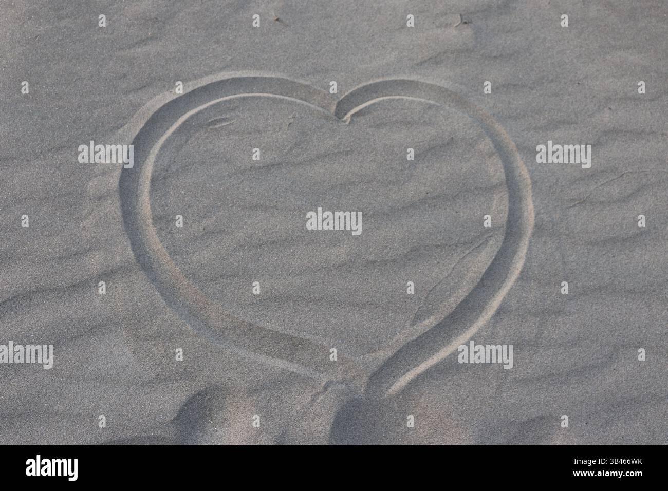 Impronta cardiaca nella sabbia. Un colpo di sabbia dall'alto verso il basso con una forma a cuore incisa su di esso. La consistenza della sabbia è chiaramente visibile, creando un senso di profondità e r Foto Stock
