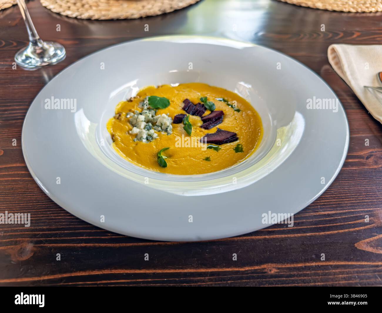 Zuppa di mais gourmet con formaggio blu, barbabietola arrostita ed erbe in una ciotola bianca. Zuppa di mais giallo cremosa servita con cagliata di formaggio blu e barbabietola Foto Stock
