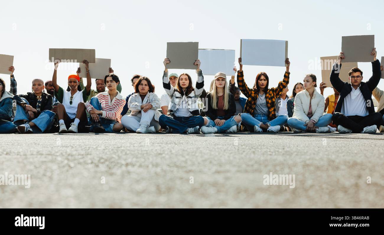 Un gruppo eterogeneo di persone, sedute sul marciapiede, partecipa a una protesta pacifica per l'azione per il clima. Hanno segni vuoti, simboleggiano l'unità Foto Stock