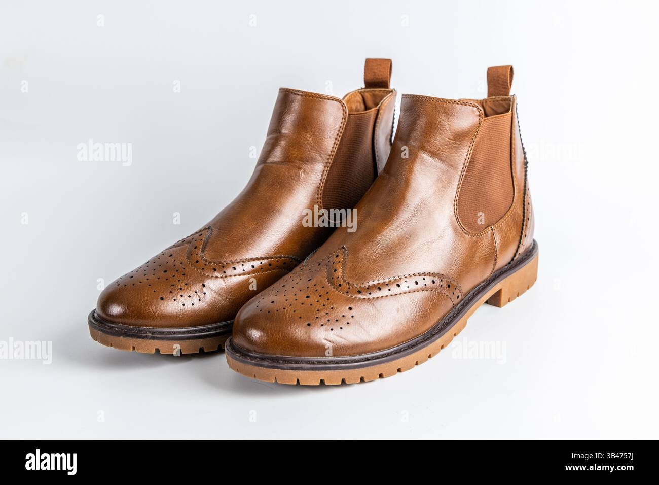 Un paio di stivali Chelsea marroni in pelle con dettagli in brogue e suola in gomma su sfondo bianco. Foto Stock
