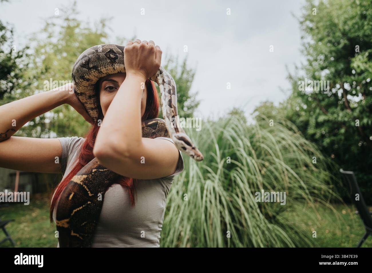 La ragazza interagisce con un grande serpente nel lussureggiante giardino verde Foto Stock
