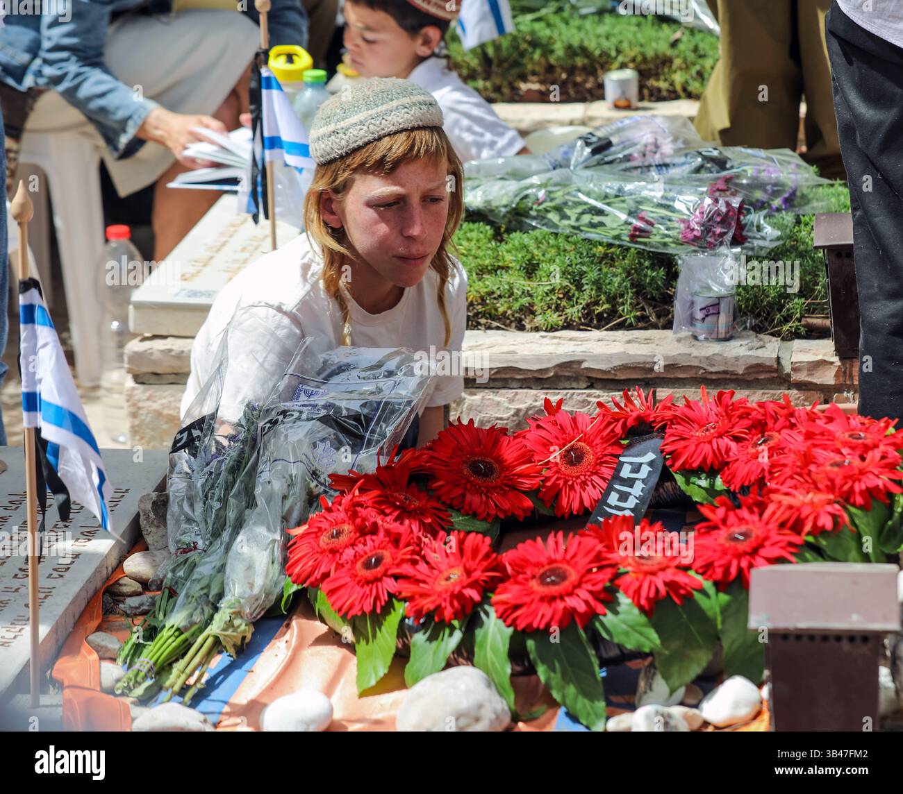 Gerusalemme, Israele. 30 aprile 2025. Israele sta commemorando il Memorial Day per i soldati caduti nelle cerimonie nei cimiteri militari. Un ragazzo con una kippah è seduto accanto a una tomba ricoperta di fiori rossi. Crediti: Yoram Biberman/Alamy Live News. Foto Stock