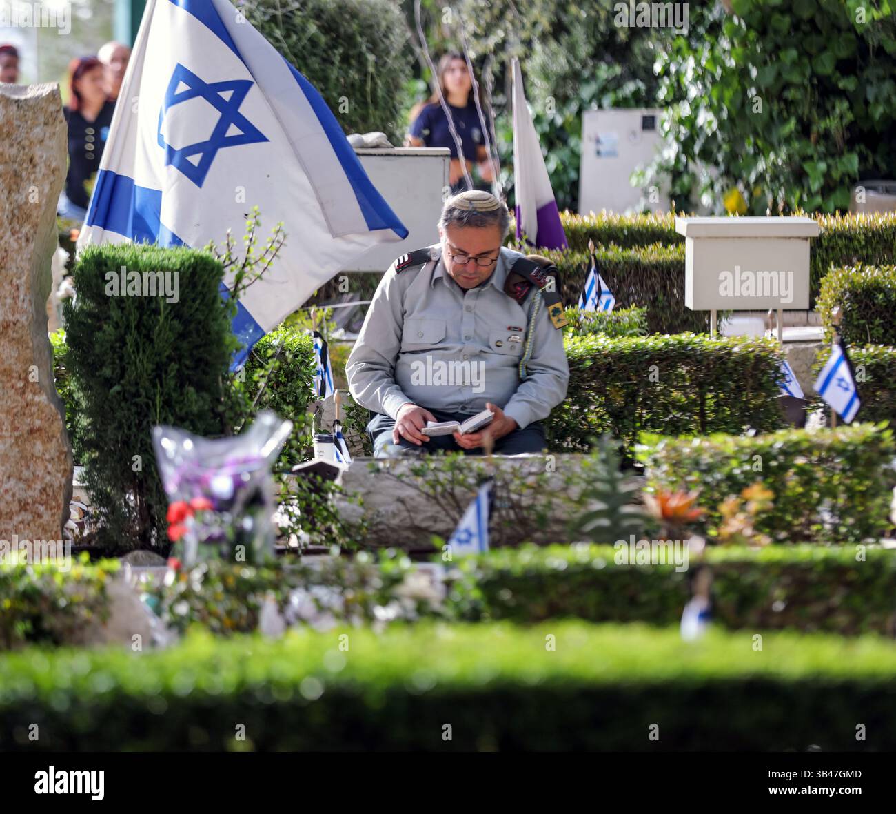 Gerusalemme, Israele. 30 aprile 2025. Israele sta commemorando il Memorial Day per i soldati caduti nelle cerimonie nei cimiteri militari. Un ufficiale seduto accanto a una tomba, pregando. Dietro di lui c'è una grande bandiera israeliana. Crediti: Yoram Biberman/Alamy Live News. Foto Stock