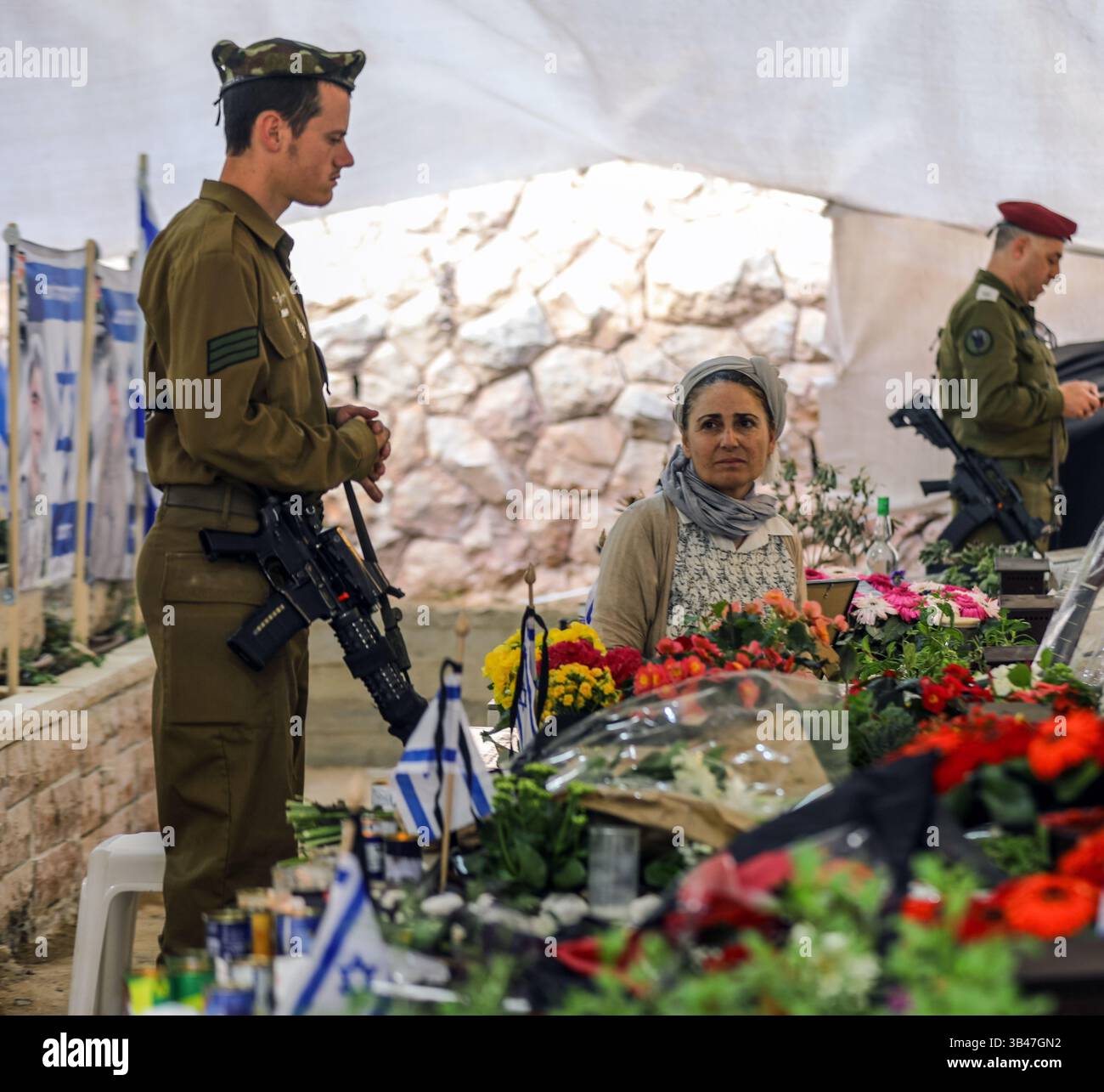 Gerusalemme, Israele. 30 aprile 2025. Israele sta commemorando il Memorial Day per i soldati caduti nelle cerimonie nei cimiteri militari. Una madre è seduta accanto a una tomba, e un giovane soldato armato è in piedi accanto a lei. Crediti: Yoram Biberman/Alamy Live News. Foto Stock
