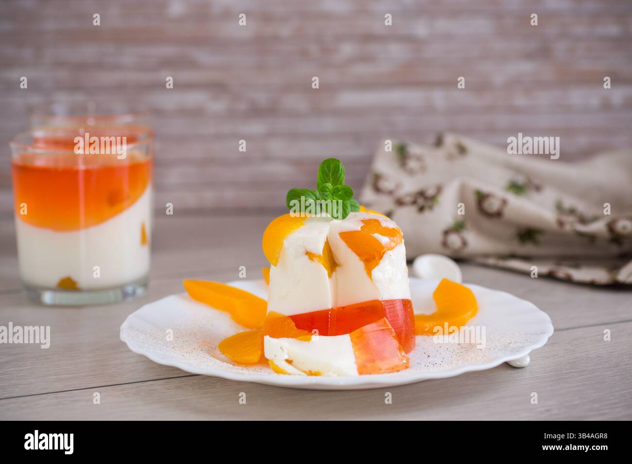 Dessert di frutta a strati con gelatina, panna e menta fresca su un tavolo di legno. Foto Stock