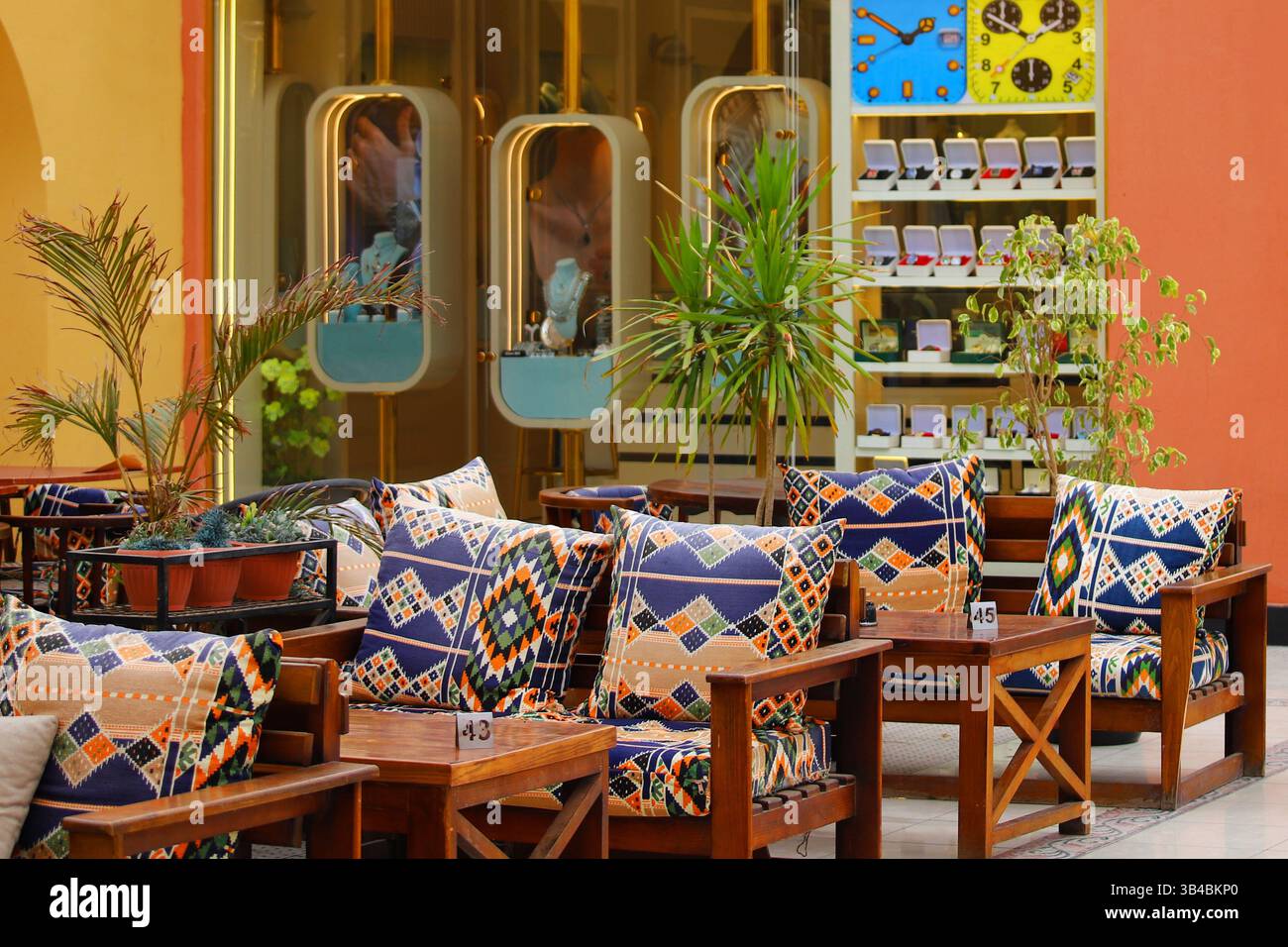 Tradizionale caffè egiziano all'aperto a Hurghada, con vivaci cuscini geometrici e piante tropicali sullo sfondo. Foto Stock