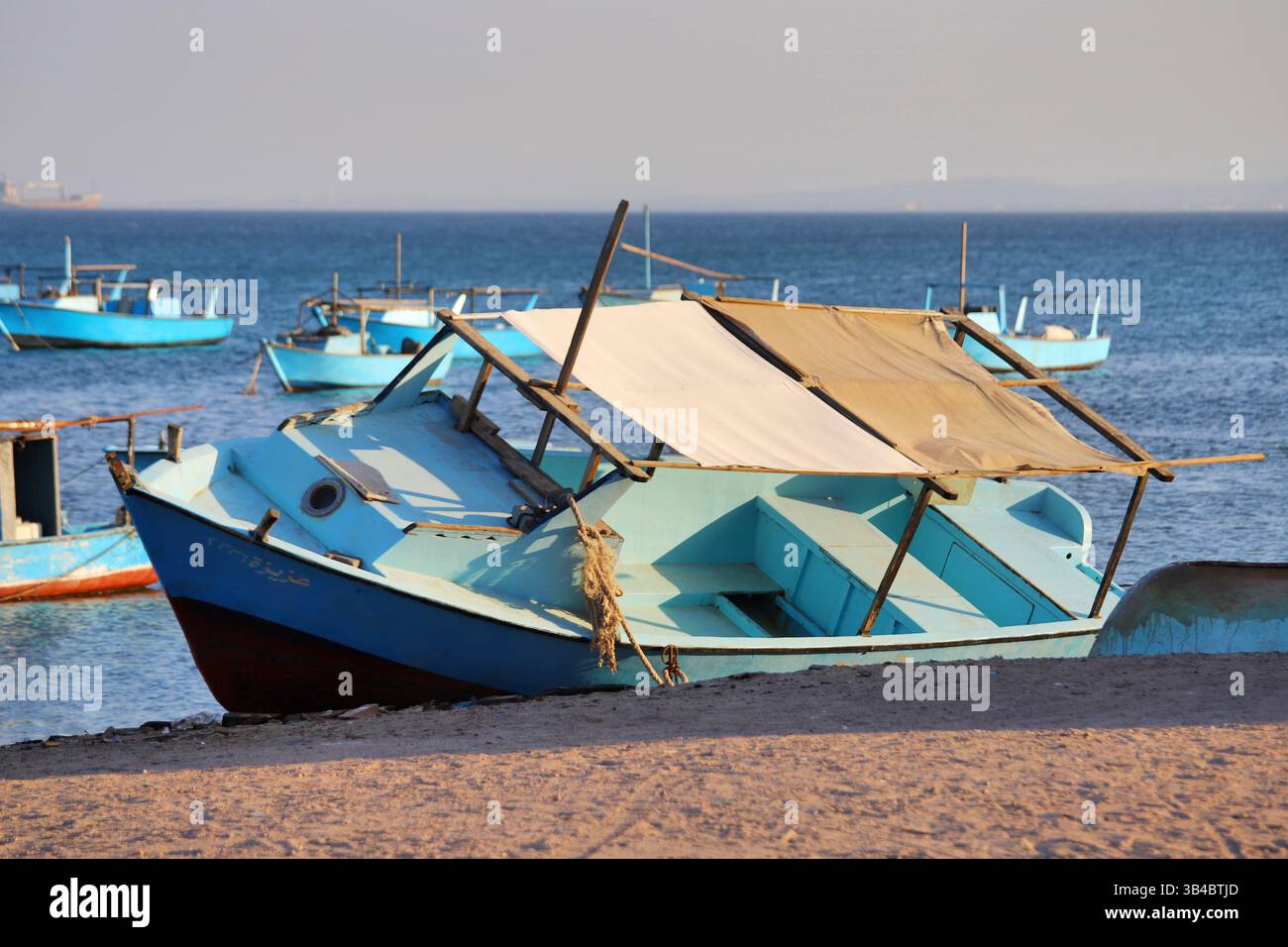 Barca da pesca con tela sulla costa sabbiosa di Safaga, Egitto, barche del Mar Rosso che galleggiano sullo sfondo sotto la luce calda del sole. Foto Stock