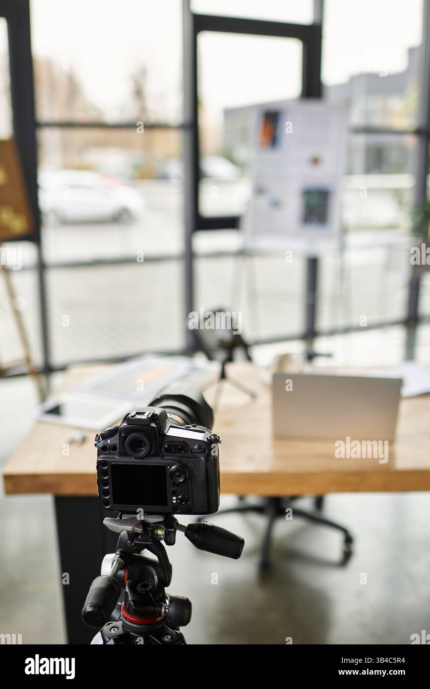 Un'area di lavoro ben organizzata mostra una fotocamera su un cavalletto accanto a un laptop e proietta i materiali. Foto Stock