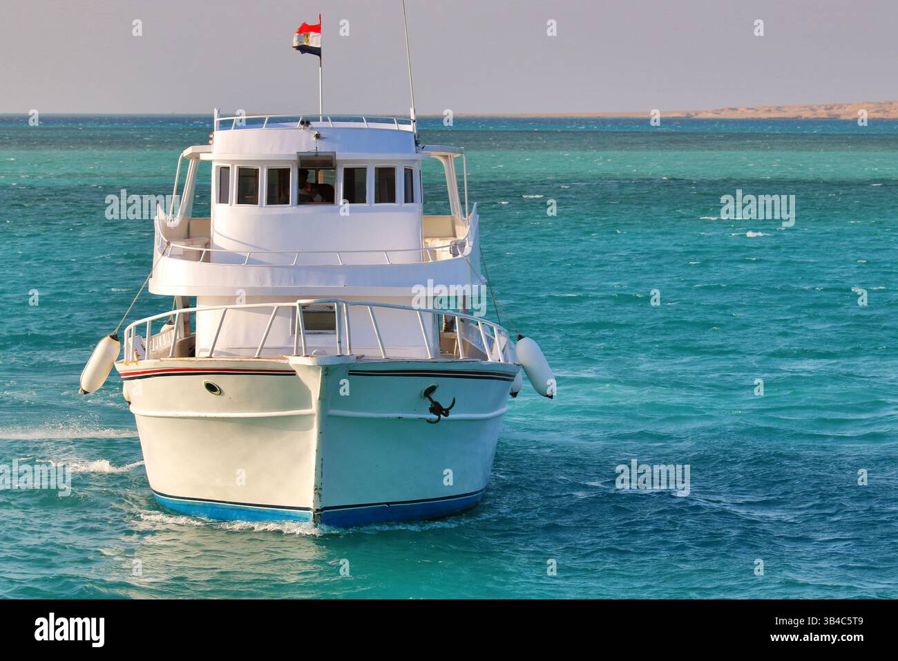 Yacht bianco con bandiera egiziana che naviga sulle acque turchesi del Mar Rosso, vicino a Hurghada, Egitto, con la costa desertica sullo sfondo. Foto Stock