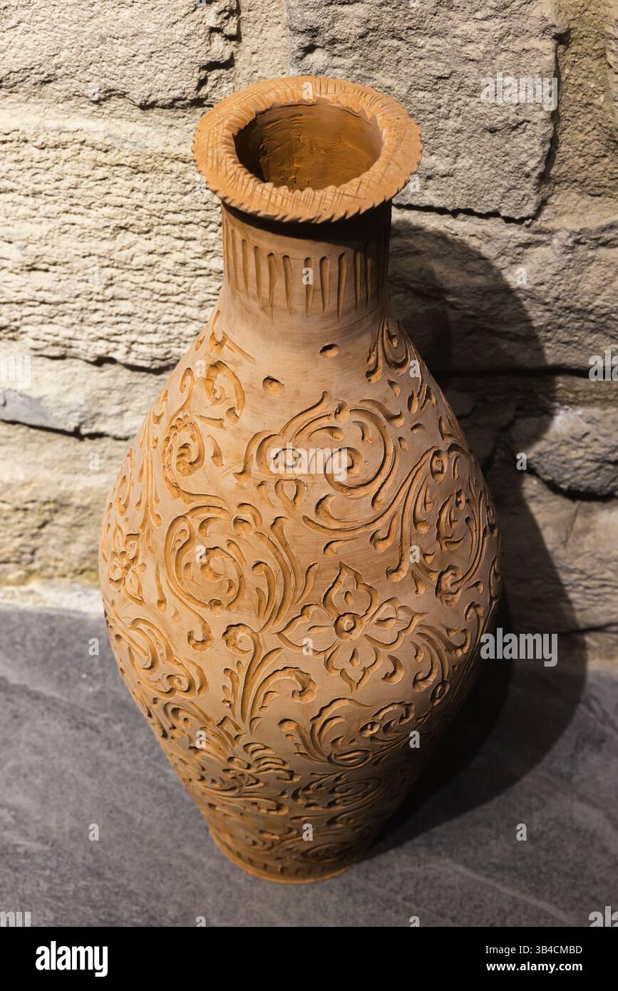 Un vaso ornamentale in ceramica caratterizzato da elaborate incisioni floreali realizzate in argilla collocate accanto ad un muro di pietra Foto Stock