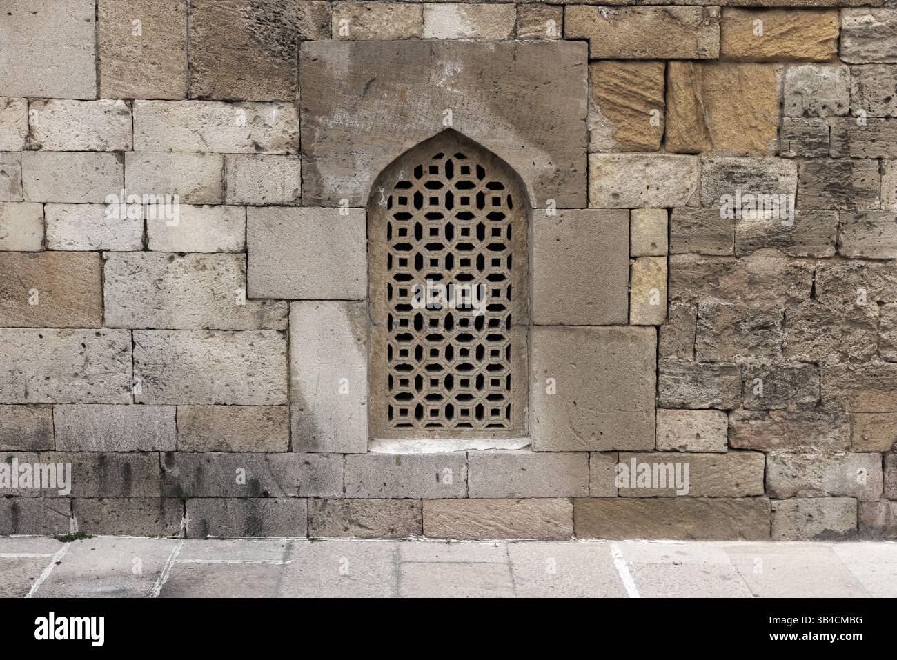 Storica parete in pietra con una finestra decorativa splendidamente realizzata con un design arabesco. La struttura mette in mostra le tradizionali tecniche murarie Foto Stock