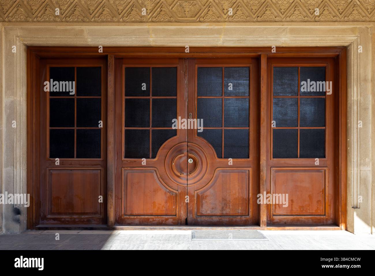 Belle porte doppie in legno con motivo geometrico simmetrico, pannelli di vetro scuro e intricate incisioni. Il design trasmette eleganza, senza tempo Foto Stock